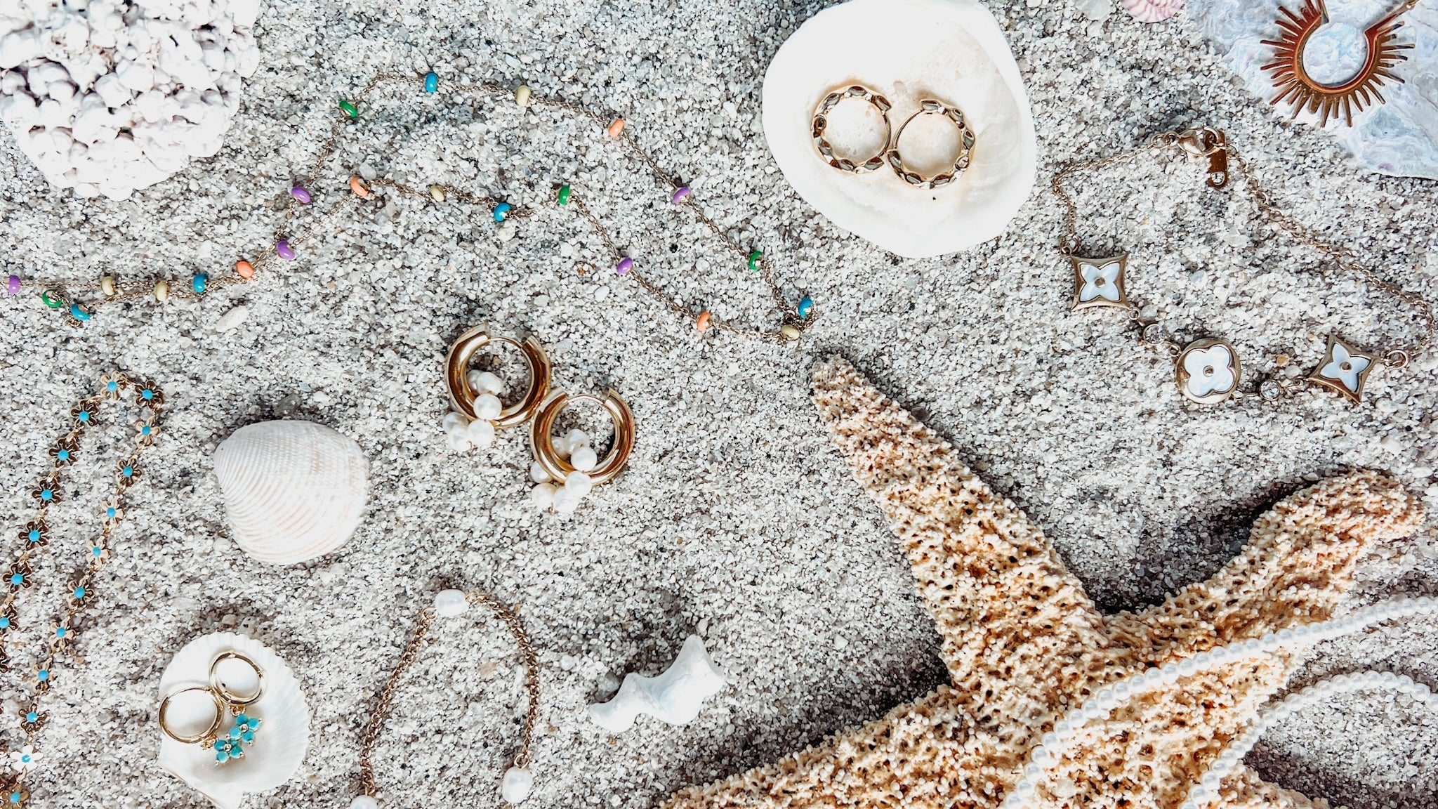Jewelry that is sitting in a pile of sand with seashells 