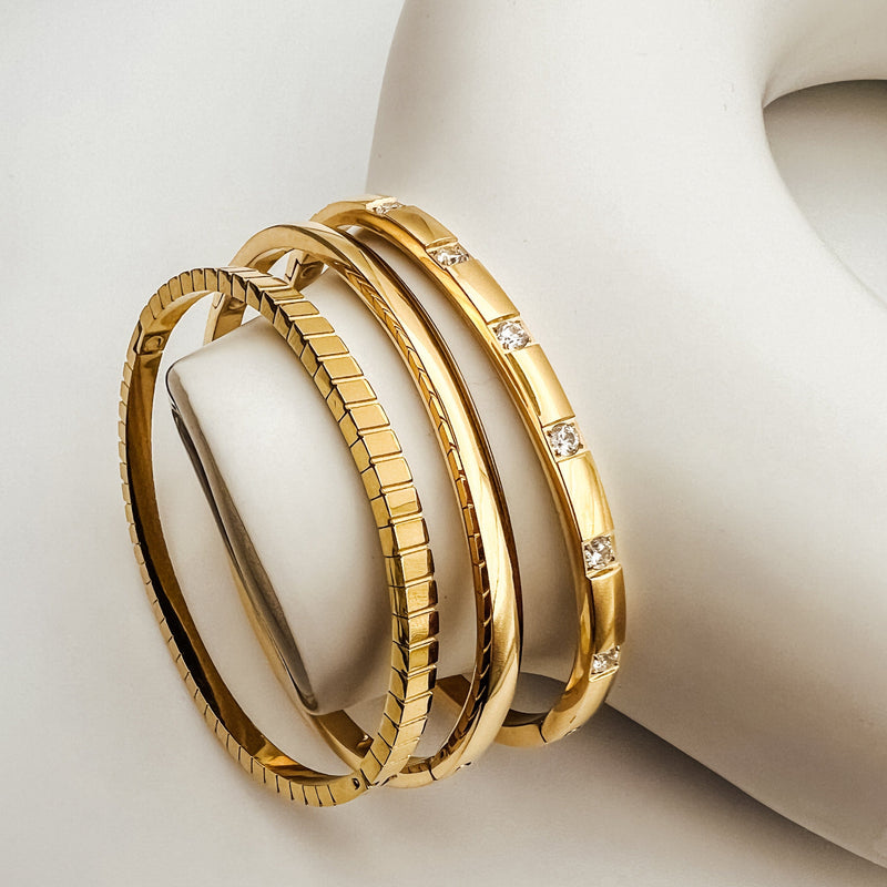 Three gold bangle bracelets resting on a white vase
